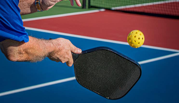 Over the shoulder shot of man hitting a pickleball with a paddle